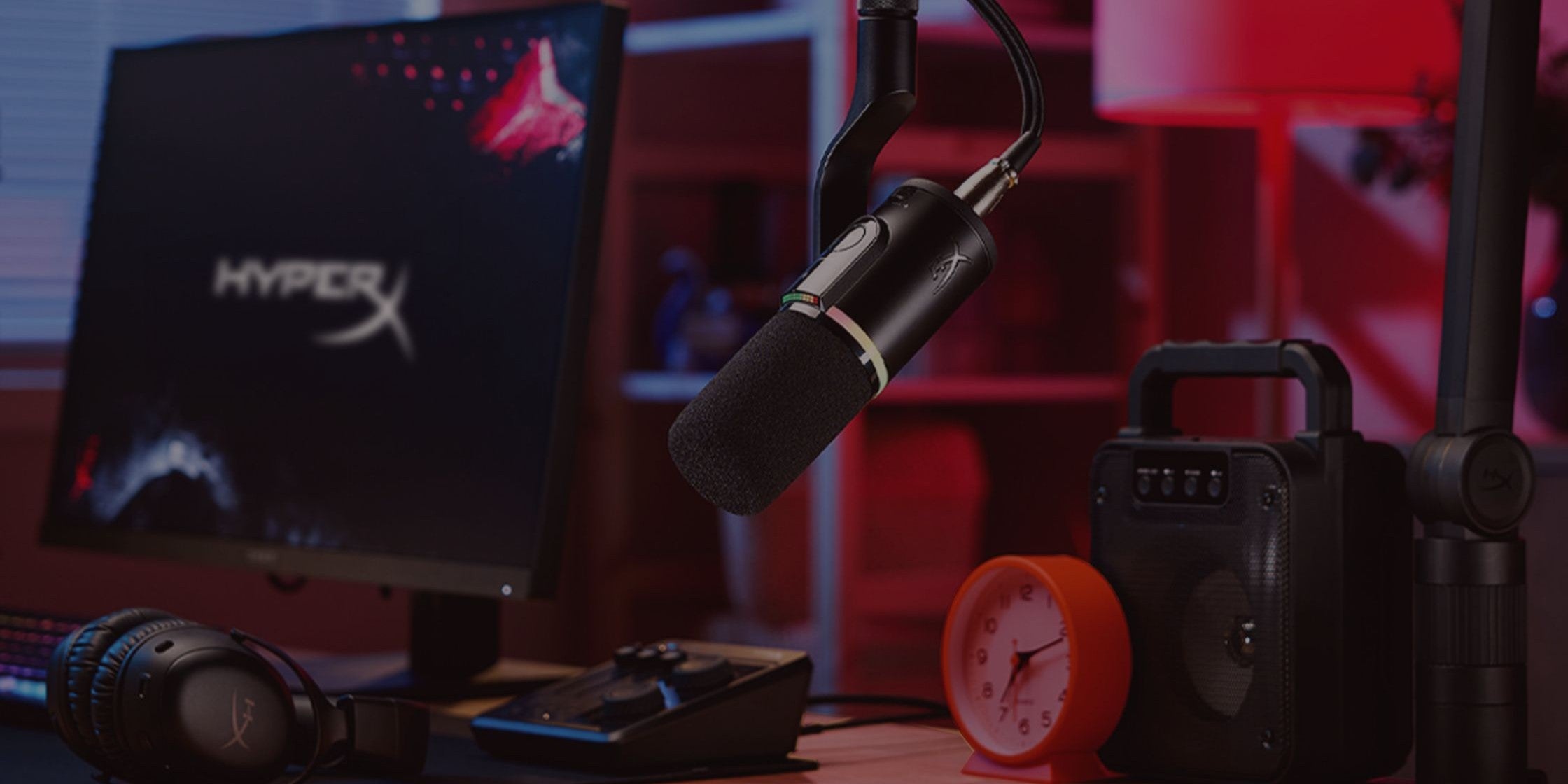 Gaming setup with HyperX monitor, microphone, and speakers on a desk.